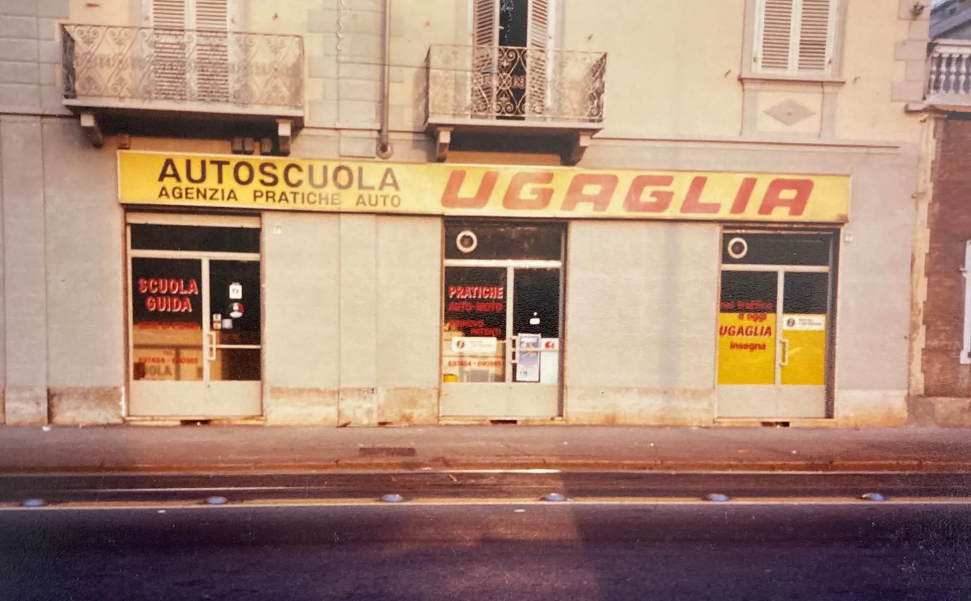El escaparate de Autoscuola Ugaglia en 1980, con el largo rótulo amarillo “Autoscuola – Agenzia pratiche auto – Ugaglia”